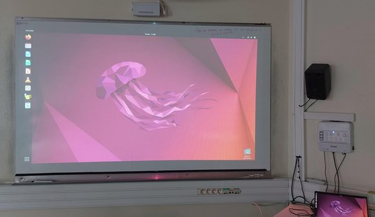 Photo d'un bureau d'ordinateur en tête de classe avec Ubuntu vidéoprojeté. On reconnait le fond d'écran violet